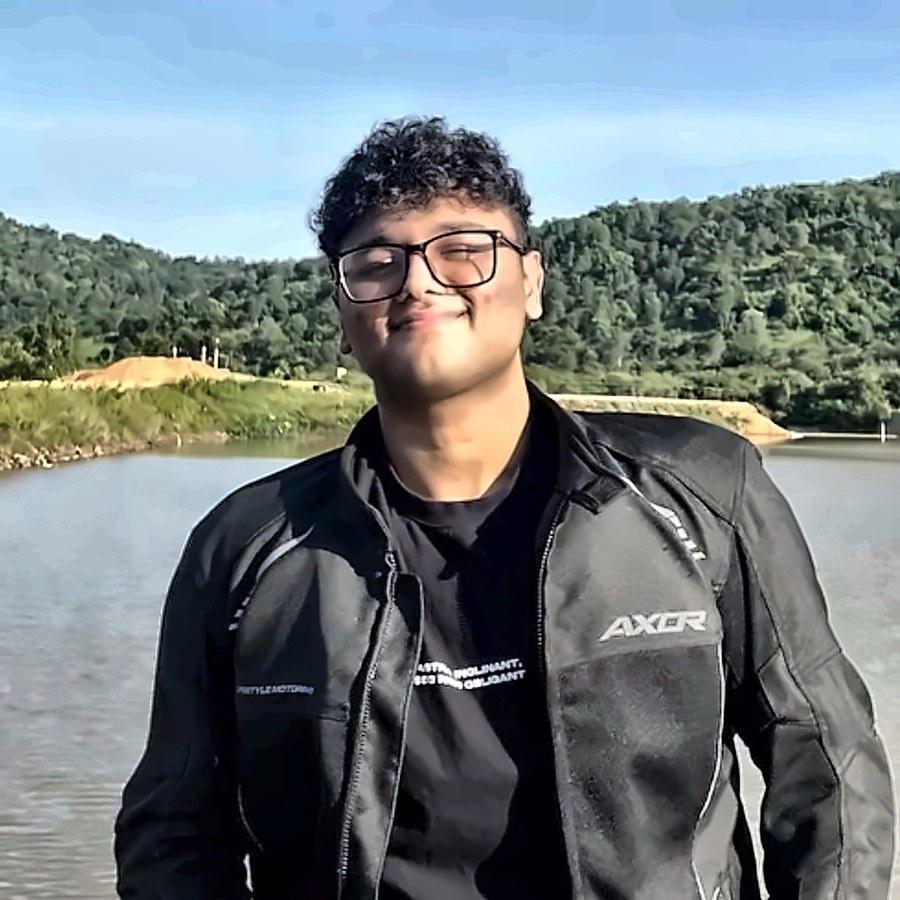 Aditya Murali, smiling, by a lake with green hills behind